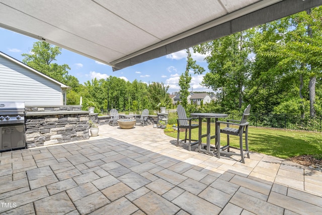 view of patio featuring area for grilling, a fire pit, exterior kitchen, outdoor dining area, and view of wooded area
