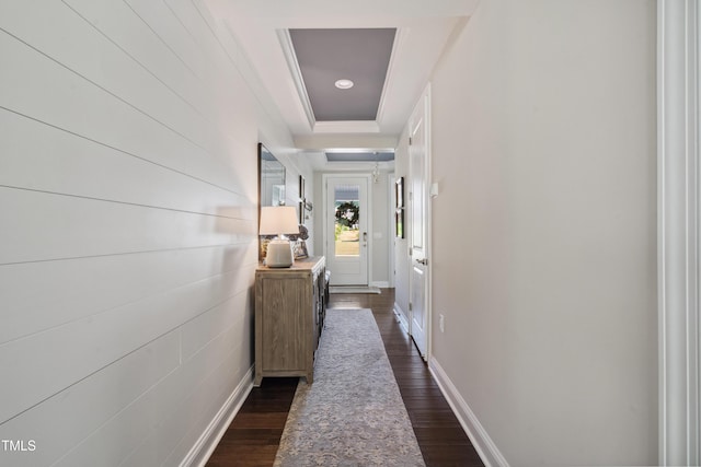 corridor with dark wood-style floors, a tray ceiling, and baseboards