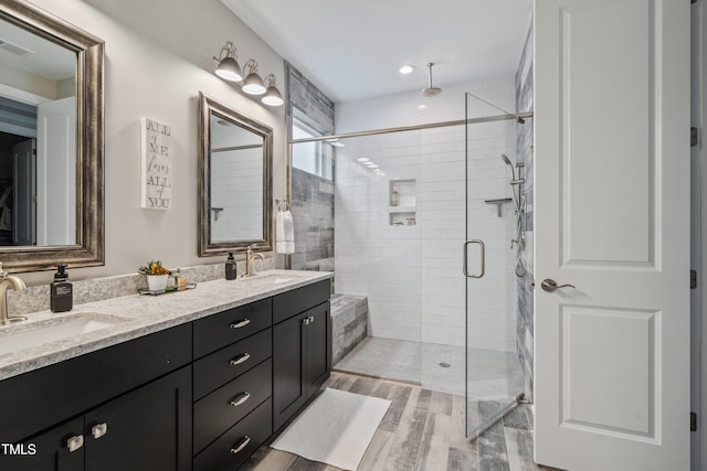 bathroom with a shower stall, double vanity, and wood finished floors
