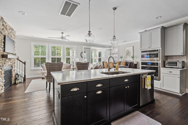 kitchen featuring a sink, open floor plan, crown molding, stainless steel appliances, and a kitchen island with sink