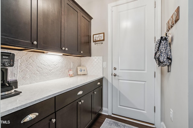 kitchen featuring dark brown cabinets, dark wood finished floors, decorative backsplash, and light stone counters
