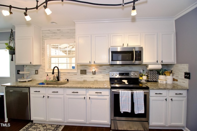 kitchen with appliances with stainless steel finishes, ornamental molding, a sink, white cabinetry, and tasteful backsplash