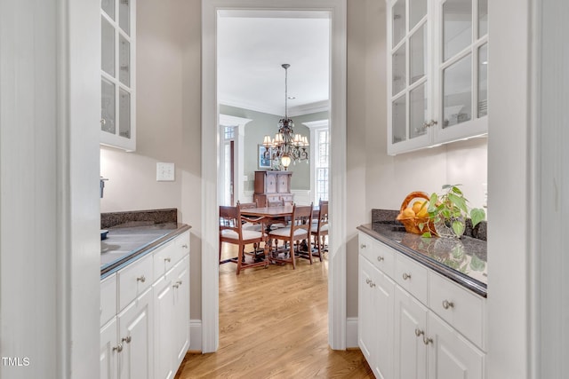 kitchen featuring dark countertops, a chandelier, white cabinets, light wood-style flooring, and ornamental molding