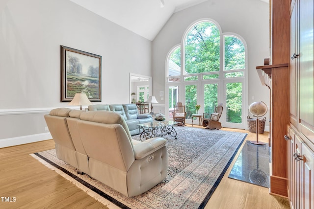 living room featuring high vaulted ceiling, light wood finished floors, and baseboards