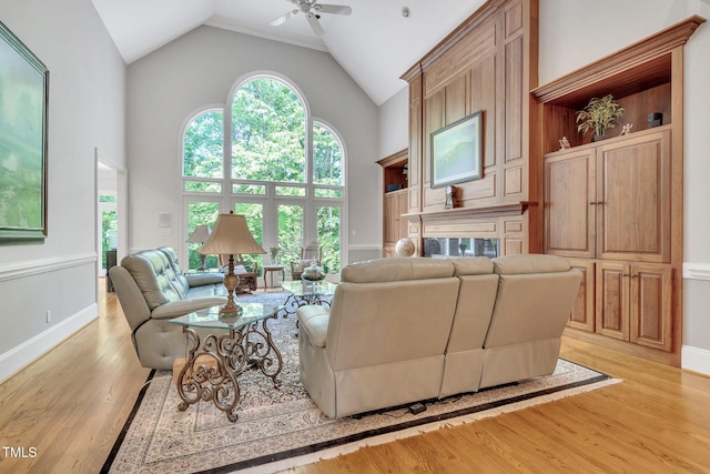 living room featuring ceiling fan, light wood finished floors, high vaulted ceiling, and baseboards