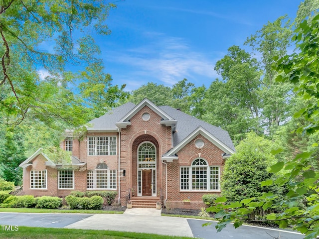colonial home featuring brick siding and a shingled roof