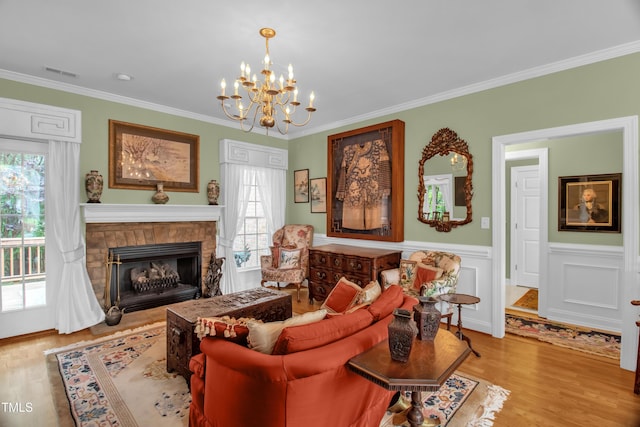 living room featuring a chandelier, wood finished floors, ornamental molding, a stone fireplace, and a wainscoted wall