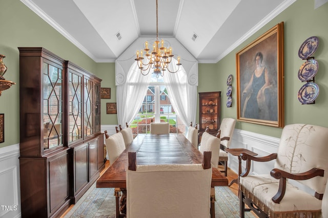 dining room featuring a chandelier, a wainscoted wall, vaulted ceiling, a decorative wall, and ornamental molding