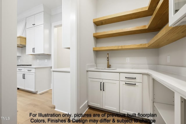 kitchen with a sink, tasteful backsplash, white cabinetry, light wood-type flooring, and light countertops