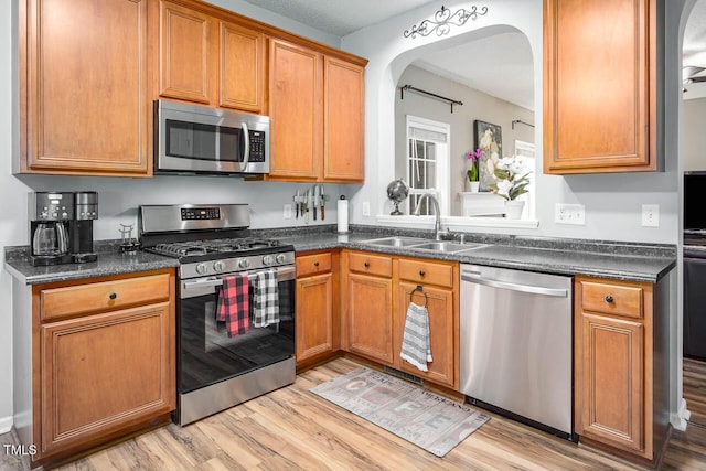 5629 Yates Garden Ln, Raleigh, NC 27606 - kitchen featuring appliances with stainless steel finishes, arched walkways, a sink, light wood finished floors, and dark countertops