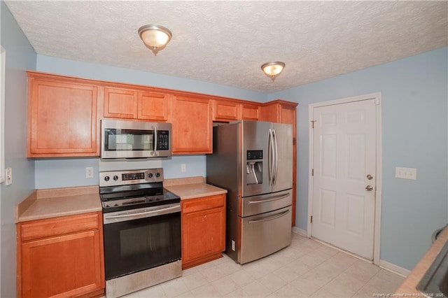 kitchen featuring appliances with stainless steel finishes, light countertops, brown cabinetry, and a textured ceiling