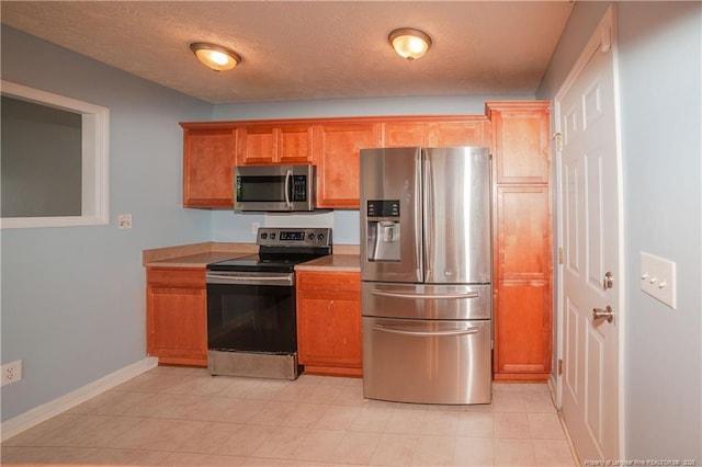 kitchen with stainless steel appliances, baseboards, brown cabinets, light countertops, and a textured ceiling