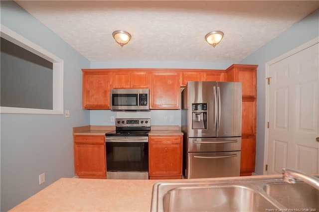 kitchen with appliances with stainless steel finishes, a sink, light countertops, and brown cabinetry