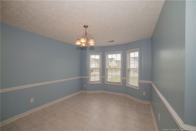empty room with a chandelier, a textured ceiling, and baseboards