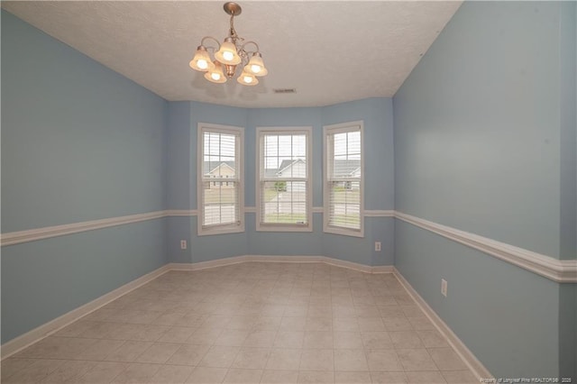 unfurnished room featuring a chandelier, a textured ceiling, and baseboards
