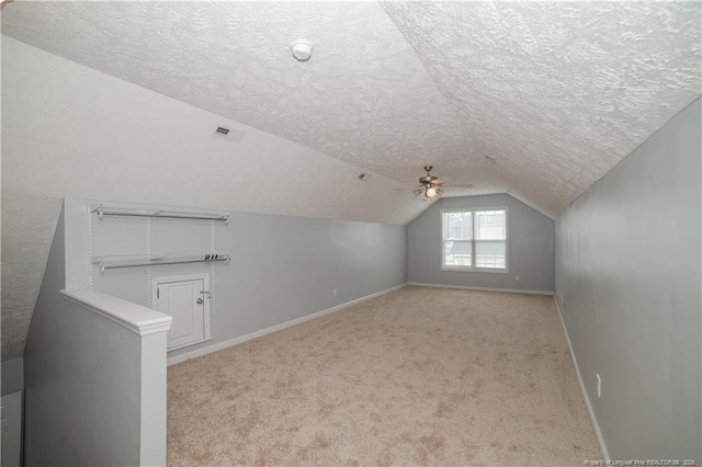 bonus room featuring a textured ceiling, baseboards, light colored carpet, vaulted ceiling, and a ceiling fan