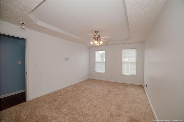 spare room featuring a tray ceiling, a textured ceiling, light carpet, a ceiling fan, and baseboards