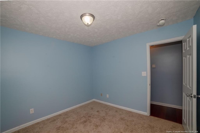 spare room featuring carpet flooring, a textured ceiling, baseboards, and a smoke detector