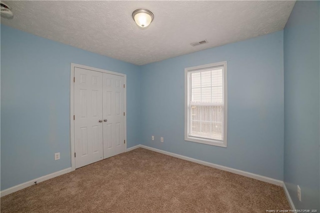 unfurnished bedroom featuring a textured ceiling, carpet flooring, a closet, and baseboards