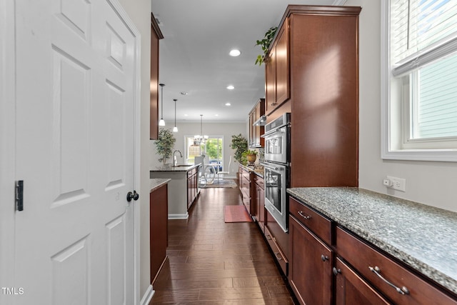 kitchen with dark wood-style flooring, recessed lighting, double oven, light stone counters, and decorative light fixtures
