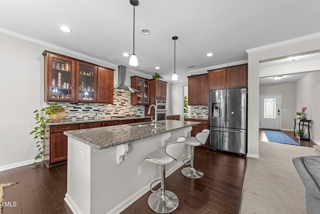 kitchen featuring appliances with stainless steel finishes, wall chimney exhaust hood, a sink, a kitchen breakfast bar, and crown molding