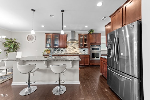 kitchen featuring appliances with stainless steel finishes, wall chimney range hood, a sink, backsplash, and a kitchen bar