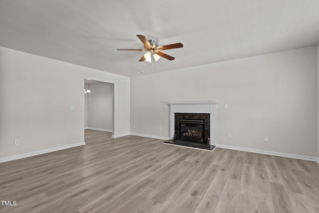 unfurnished living room with a ceiling fan, light wood-style floors, a high end fireplace, and baseboards