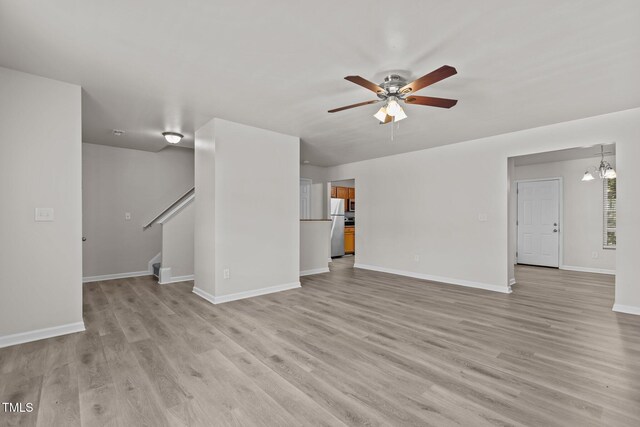 unfurnished living room featuring a ceiling fan, light wood finished floors, stairway, and baseboards