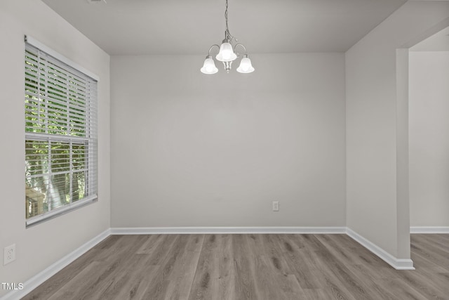 unfurnished room featuring a chandelier, wood finished floors, and baseboards