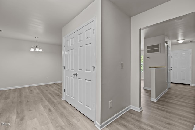 hall with a chandelier, light wood-style floors, and baseboards