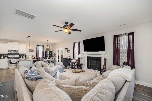 living room with dark wood-type flooring, a ceiling fan, a glass covered fireplace, and baseboards