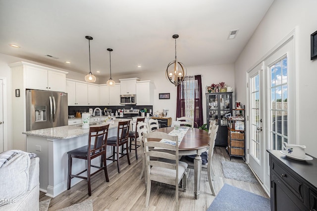 dining room with a chandelier, light wood-style flooring, recessed lighting, and french doors