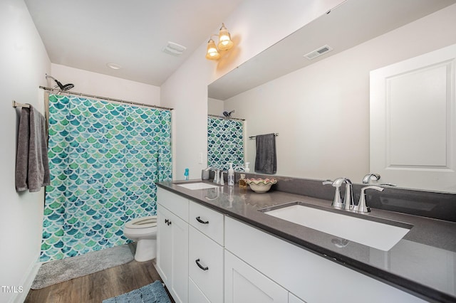 bathroom with wood finished floors, toilet, double vanity, and curtained shower