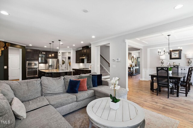 living room featuring crown molding, light wood-style flooring, recessed lighting, stairway, and a chandelier