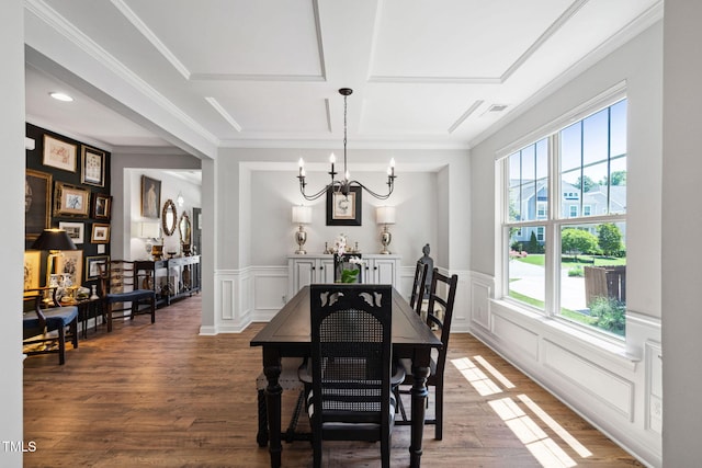 dining room featuring a chandelier, a decorative wall, wood finished floors, crown molding, and coffered ceiling