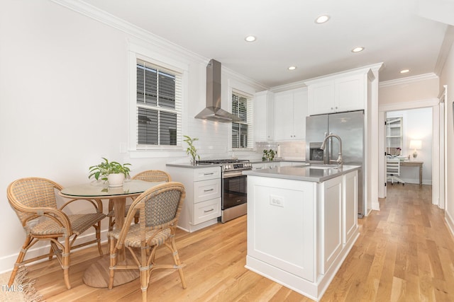 kitchen featuring gas stove, wall chimney range hood, white cabinets, an island with sink, and a sink