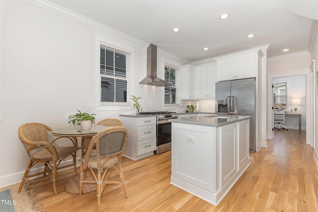 kitchen featuring stainless steel appliances, wall chimney range hood, white cabinetry, light wood-style floors, and decorative backsplash