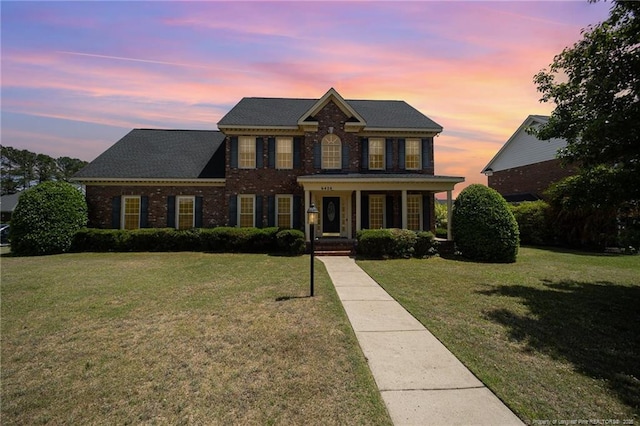 georgian-style home featuring brick siding, a front yard, and a porch