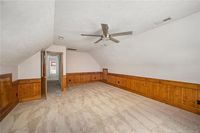 bonus room featuring a textured ceiling, a wainscoted wall, wooden walls, lofted ceiling, and a ceiling fan