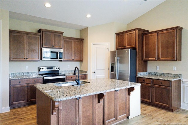 kitchen with appliances with stainless steel finishes, a sink, light wood finished floors, light stone countertops, and recessed lighting
