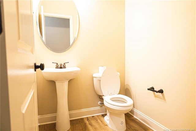 half bath featuring wood finished floors, toilet, baseboards, and a sink