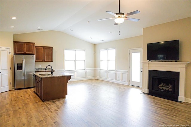 kitchen featuring stainless steel fridge with ice dispenser, open floor plan, vaulted ceiling, a sink, and light wood-style flooring