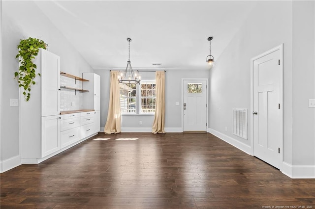 unfurnished dining area with a chandelier, vaulted ceiling, dark wood finished floors, and baseboards