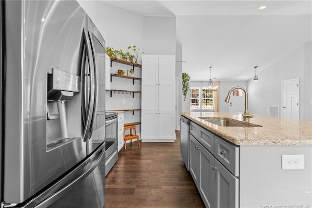 kitchen featuring stainless steel appliances, a sink, dark wood finished floors, light stone counters, and pendant lighting