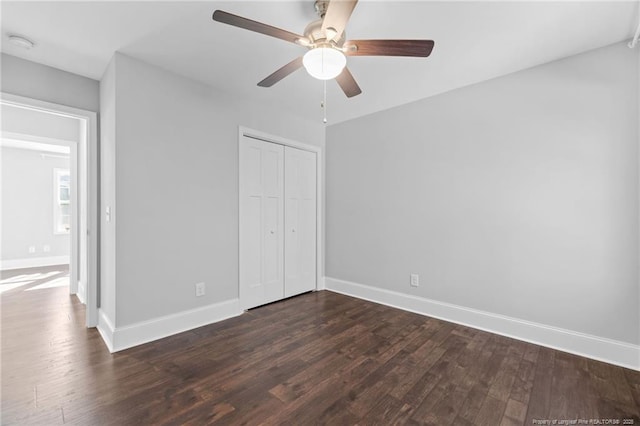 unfurnished bedroom with dark wood-type flooring, baseboards, a closet, and a ceiling fan