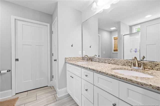 full bathroom with baseboards, a shower stall, double vanity, and wood tiled floors