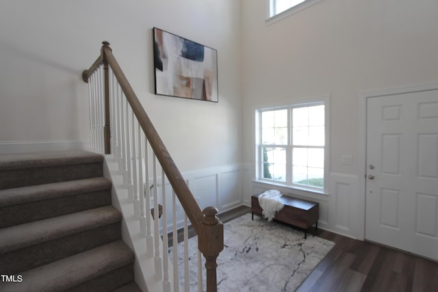 foyer entrance with wood finished floors, stairs, a wainscoted wall, and a towering ceiling