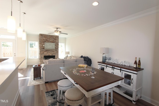 dining space featuring crown molding, a ceiling fan, dark wood-type flooring, a fireplace, and baseboards