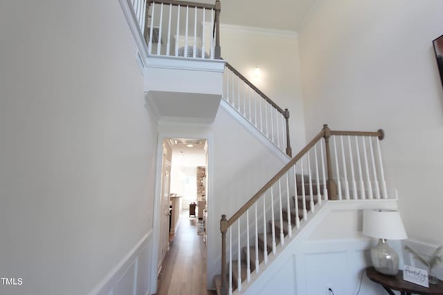 stairs featuring crown molding, a decorative wall, wood finished floors, and a high ceiling
