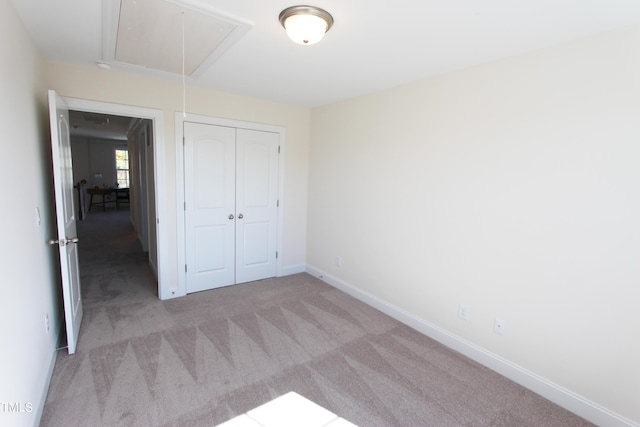 unfurnished bedroom featuring attic access, carpet floors, a closet, and baseboards
